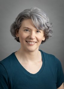 Julia Buchkina is a middle aged white woman with short gray hair and blue eyes, wearing a dark blue shirt.