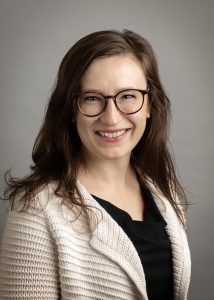 Sarah Cupp is a middle-aged Caucasian woman with long brown hair, wearing glasses and a dark shirt, light sweater, smiling at the camera.