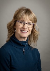 Nelson Karen Nelson is a Caucasian woman in her late 50s with blonde hair and eyeglasses. Wearing a burnt orange sweater, and silver choker necklace with a pendant.