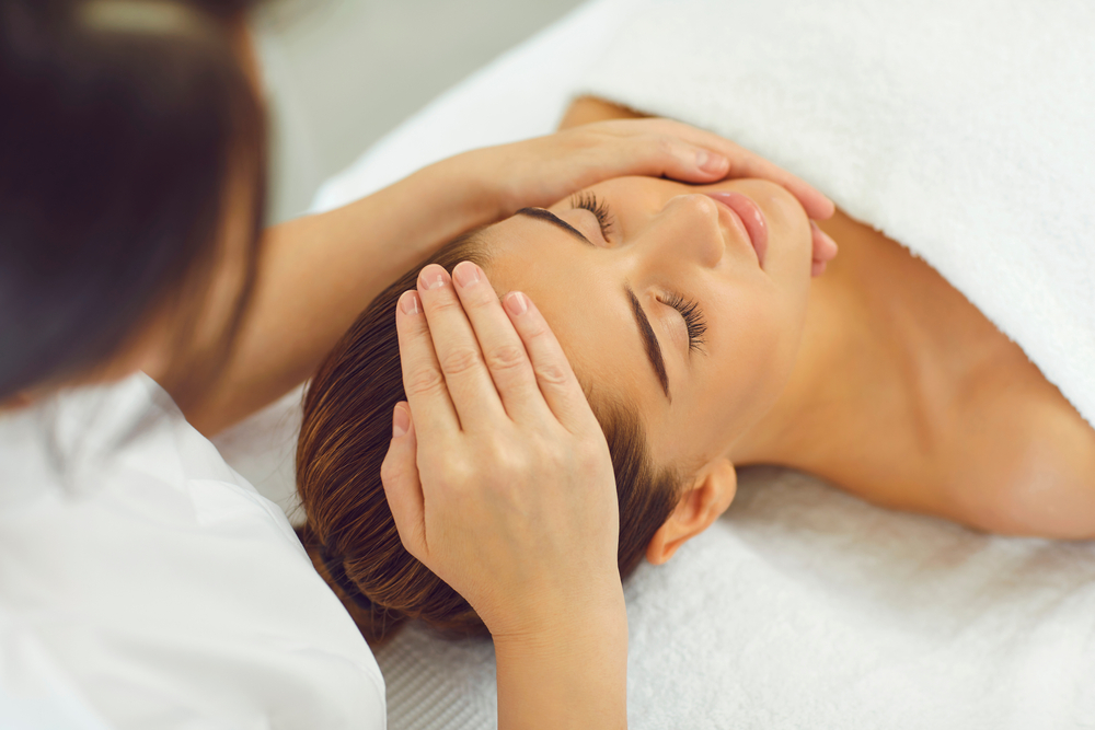 Close-up of positive woman's face receiving healing hands