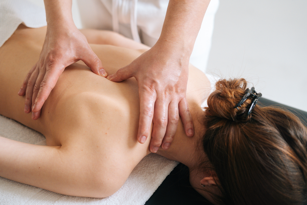 Male masseur massaging back and, shoulder blades of young woman
